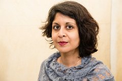 Anthony stands in front of a cream wall wearing a grey-lilac top. Their hair is in an asymmetric cut reaching to the shoulders on the near side.